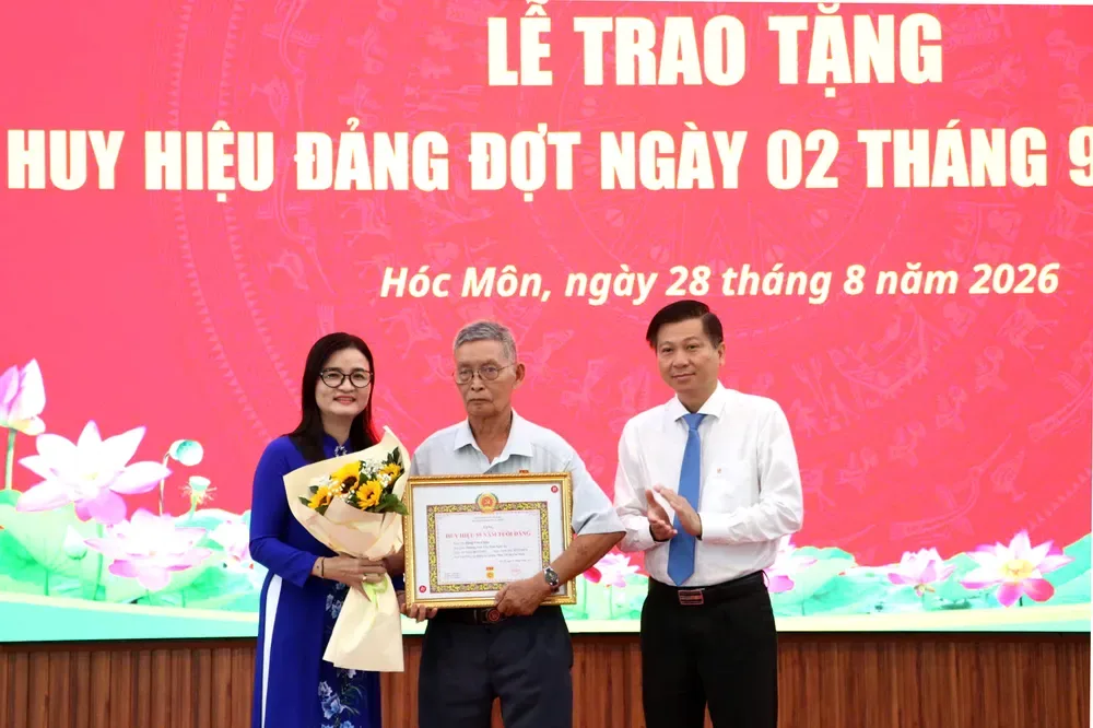 Đồng chí Trần Văn Tuấn - Ủy viên Ban Thường vụ Thành ủy, Trưởng Ban Nội chính Thành ủy TPHCM và Bí thư Đảng ủy xã Hóc Môn Lê Thị Ngọc Thanh trao Huy hiệu 55 năm tuổi Đảng đến đảng viên lão thành.